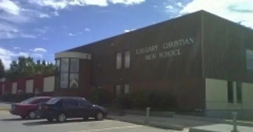 L'ampio edificio della Calgary Christian School con la scritta e un veicolo rosso in primo piano sotto un cielo nuvoloso.