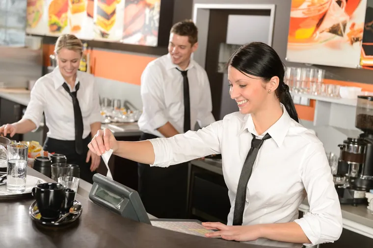 Drei Servicekräfte in weißen Hemden und Krawatten arbeiten lächelnd an der Theke eines Cafés