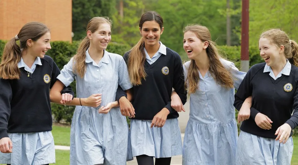 Un gruppo di giovani studentesse della St. Mary's School Ascot sorride insieme su un prato davanti a edifici e alberi.