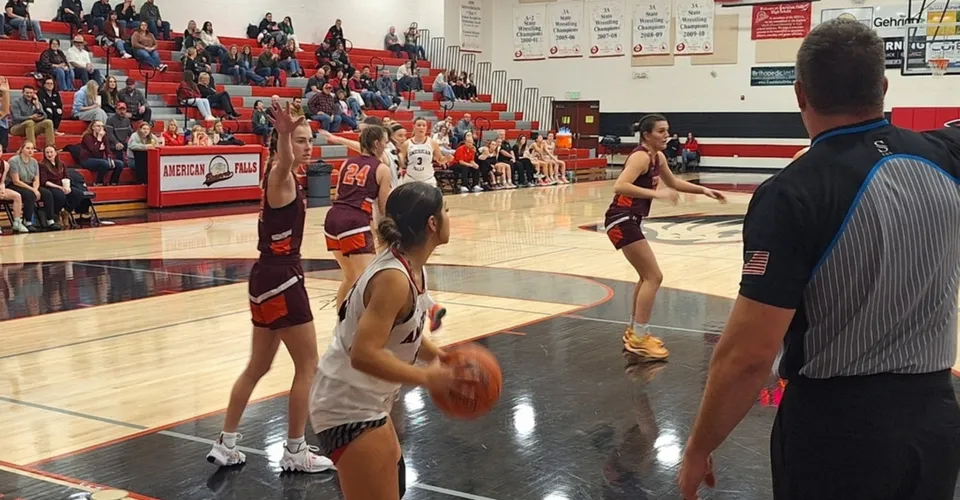Studenti della American Falls High School giocano una partita di basket nel cortile della scuola con spettatori sugli spalti.
