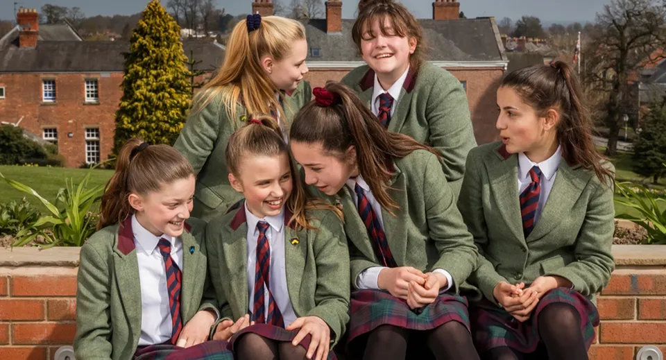 Studentesse in blazer verdi e gonne rosse sul campus della Oswestry School sono insieme e chiacchierano.