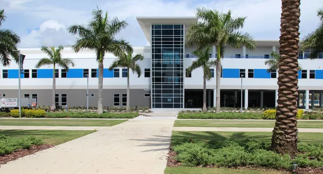 L'edificio moderno a più piani della IMG Academy con grandi finestre e palme in primo piano sotto un cielo blu.