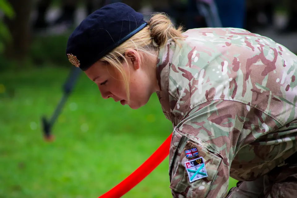 Una persona in uniforme mimetica militare sta in piedi su un prato nel campus del Plymouth College a testa bassa.