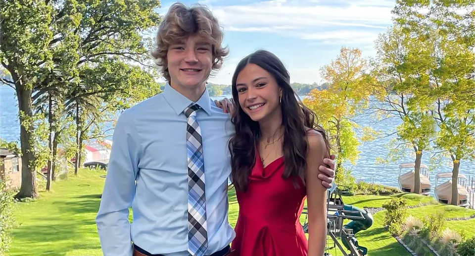 Una giovane coppia si trova insieme in un paesaggio verde all'esterno della Holy Family Catholic High School.