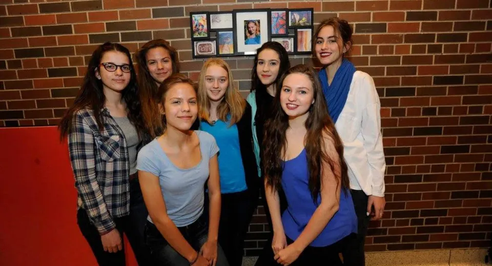 Un gruppo di studentesse sta davanti a una parete in mattoni con foto incorniciate nel campus del Silverthorn Collegiate Institute.