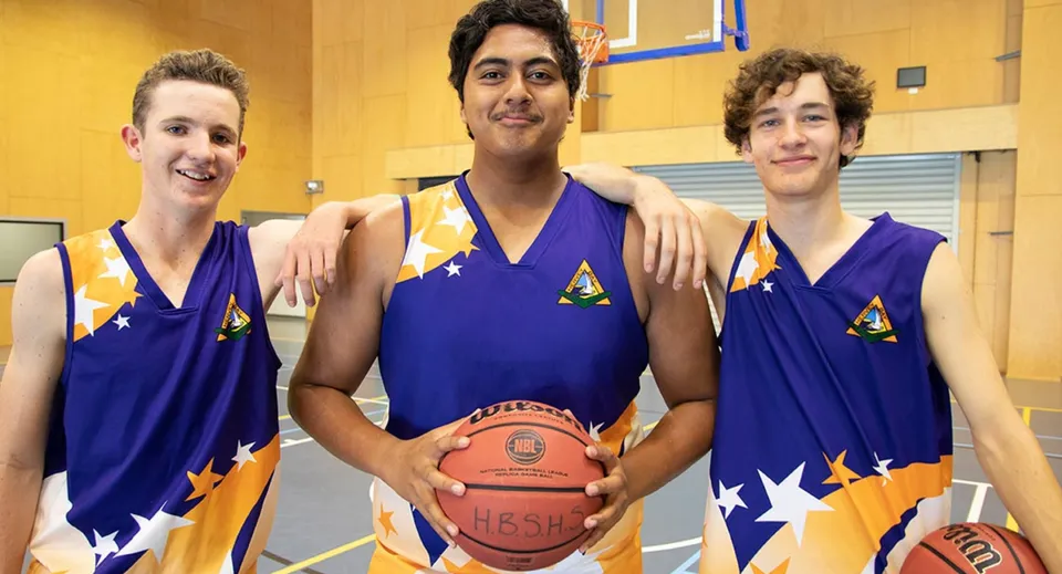 Tre studenti della Hervey Bay State High School, in divisa da basket, sono in una palestra e tengono in mano un pallone da basket.