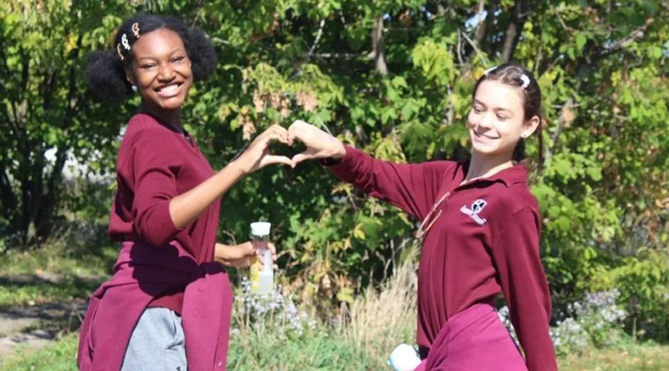 Due studentesse della Beurling Academy formano un cuore con le mani all'aperto.