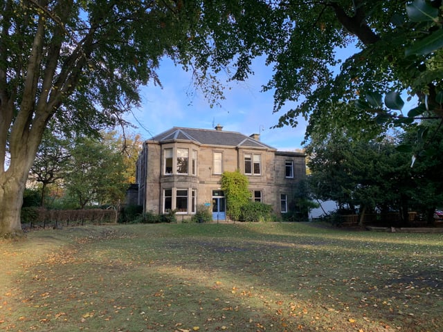Das Gebäude der Edinburgh Steiner School steht zweistöckig in einer herbstlichen Landschaft mit vielen bunten Blättern unter Bäumen.