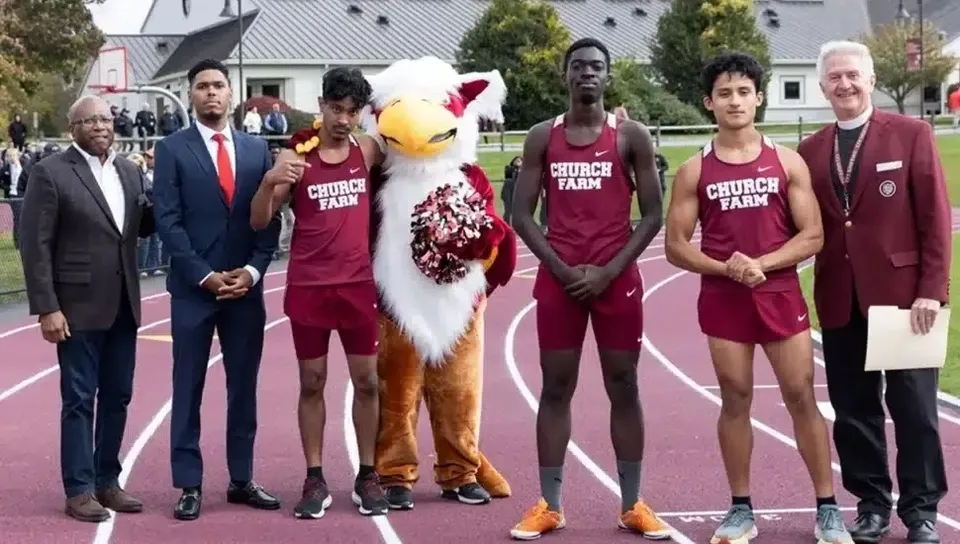 Gli studenti della Church Farm School sono in piedi insieme alla mascotte sul campo sportivo, indossando maglie uniformi.