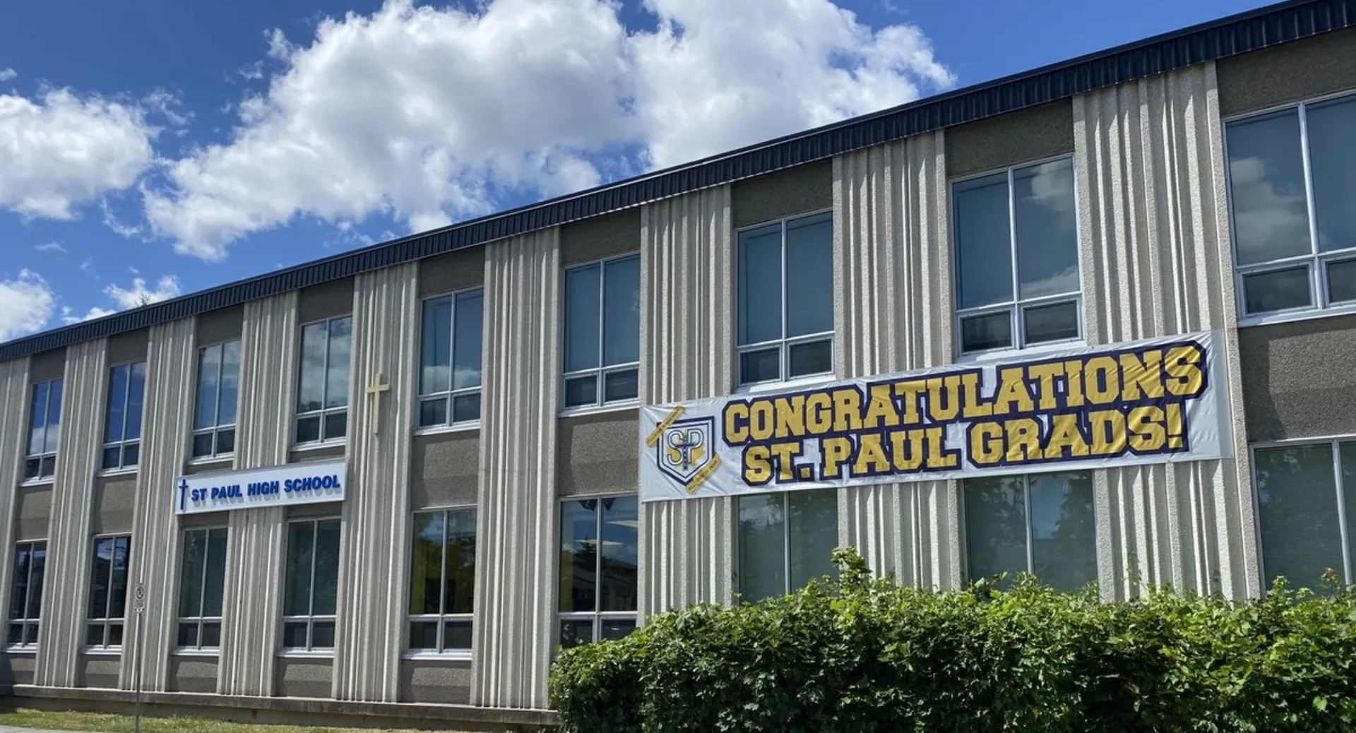 L'edificio della St. Paul High School con uno striscione che si congratula con i diplomati, davanti a un cielo blu con nuvole.