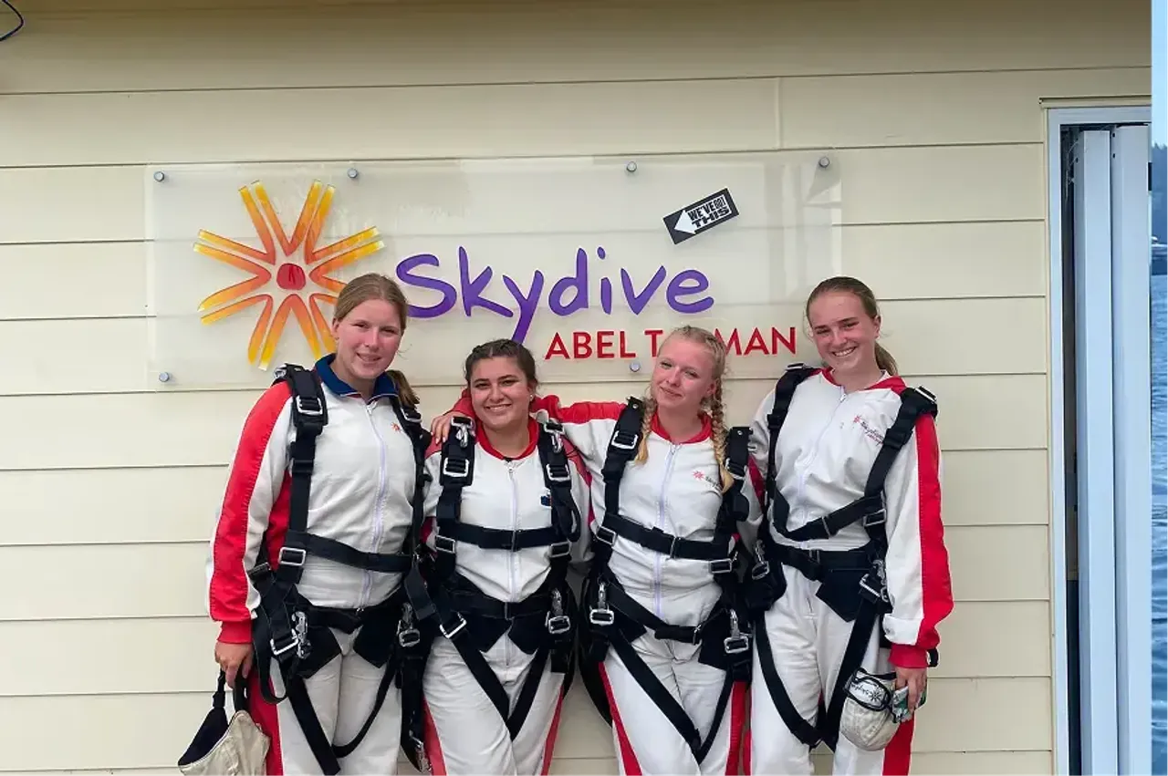Quattro studentesse in tuta da paracadutismo davanti all'insegna Skydive Abel Tasman