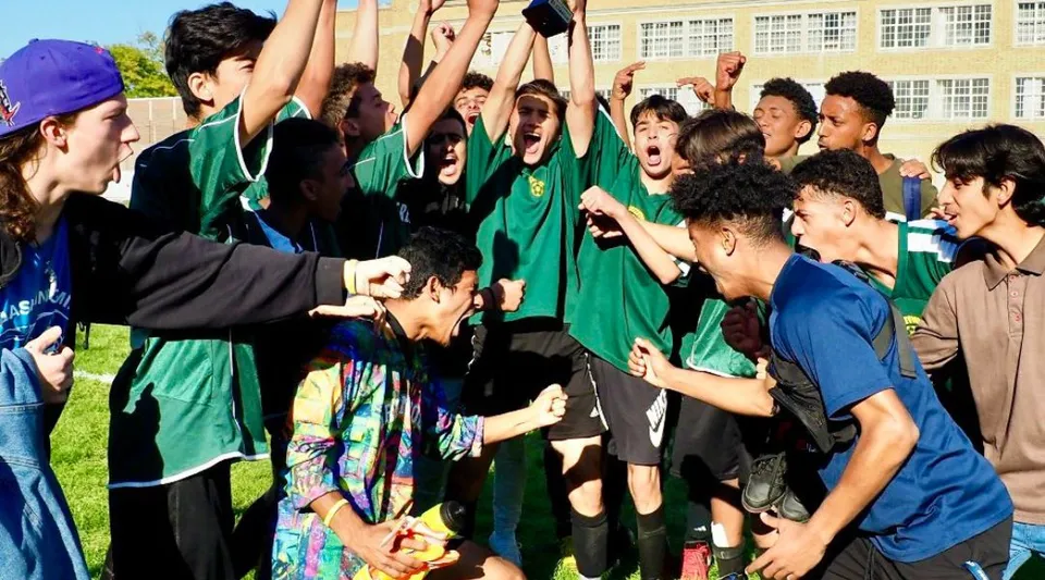 Un gruppo di studenti della Greenwood Secondary School in divise scolastiche verdi festeggia insieme davanti all'edificio scolastico.