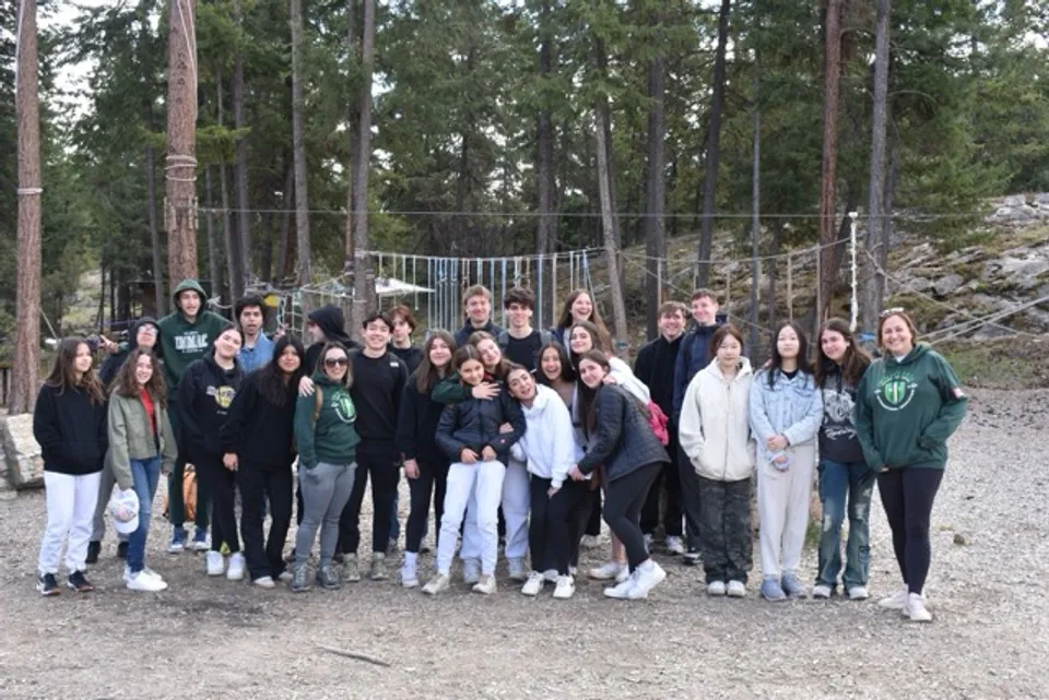 Un gruppo di studenti della Immaculata Regional School si trova insieme in un'area boschiva con un ponte sospeso sullo sfondo.