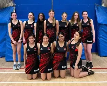 Equipo femenino de netball con equipación roja y negra posando en el pabellón