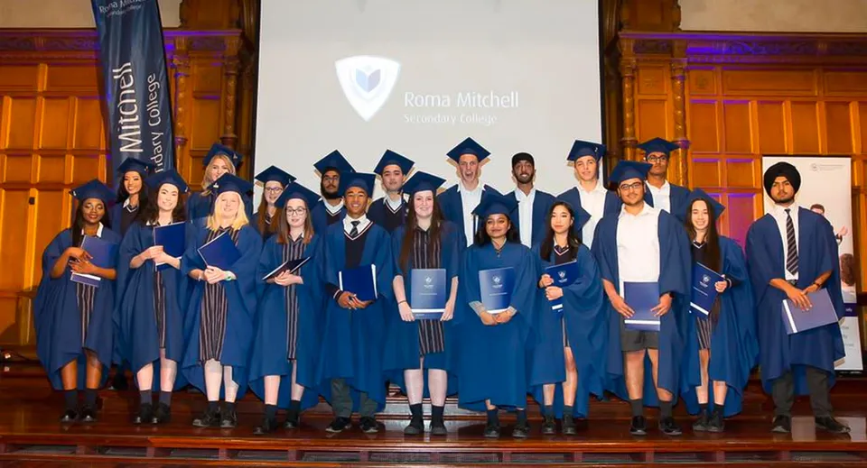 I diplomati in toga blu sono sul palco davanti a uno schermo con il logo del Roma Mitchell Secondary College.