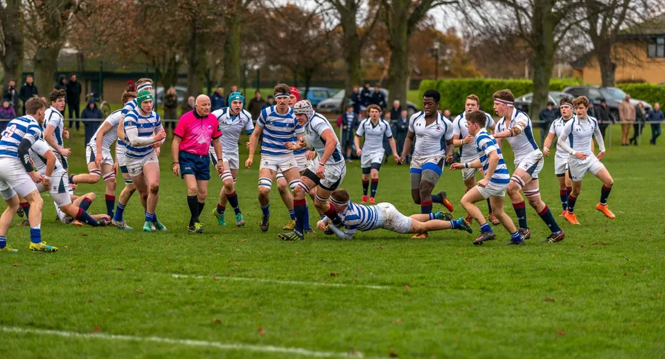 Una partita di rugby con giocatori in maglia a strisce si svolge sul campo in erba della Oundle School.