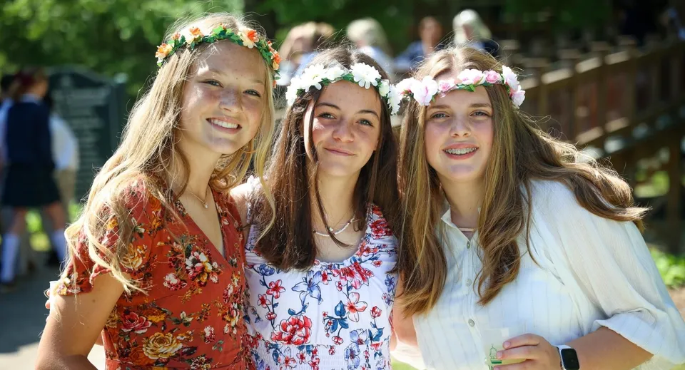 Tre studentesse con corone di fiori sorridono all'aperto nel campus della Rabun Gap-Nacoochee School.
