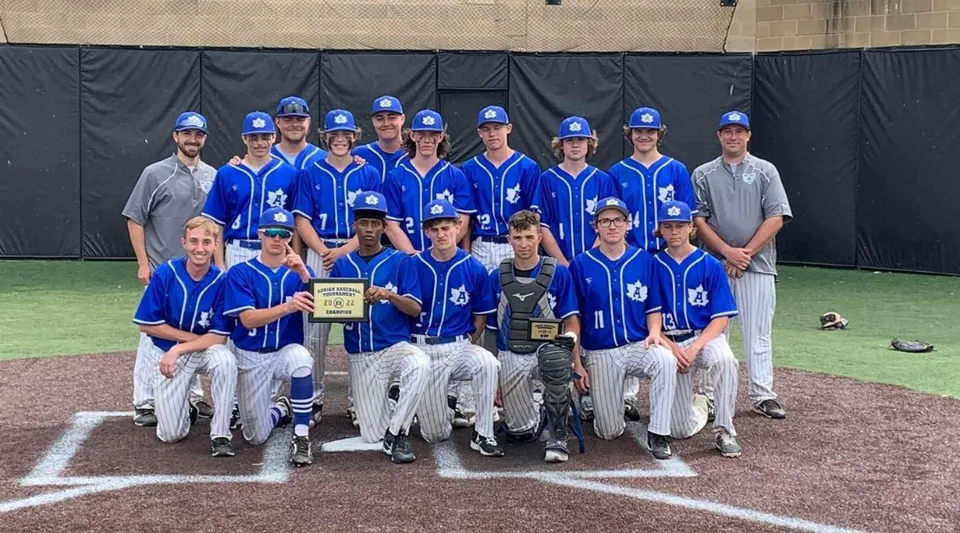 Un gruppo di giocatori di baseball in divisa blu e bianca si trova sul campo da baseball della Adrian High School.