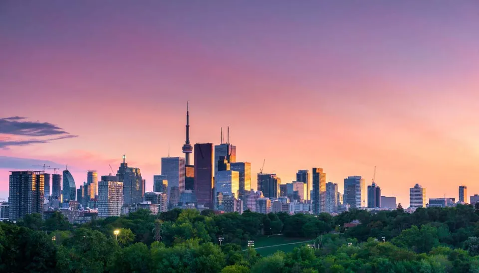 Un vivace paesaggio urbano con grattacieli al tramonto, circondato da una rigogliosa vegetazione, rappresentato senza alcun riferimento diretto alla Central Toronto Academy.