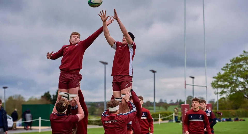 Due studenti in maglia rossa saltano per prendere la palla sul campo da calcio del Denstone College.