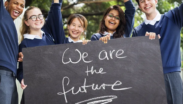 Lachende Schülerinnen und Schüler in Schuluniform halten eine Tafel mit der Aufschrift We are the future
