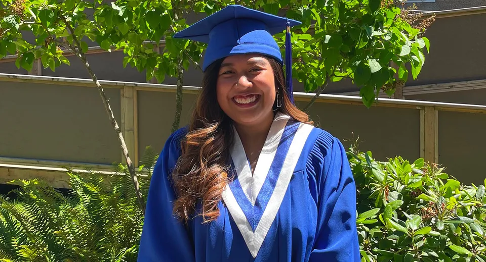 Una diplomanda con la toga blu si trova davanti a un giardino verde nel campus del South Hill Education Centre.
