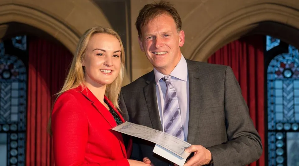 Un uomo e una donna in abito formale sono in piedi davanti a vetrate colorate nel campus dell'Abbey College Manchester.