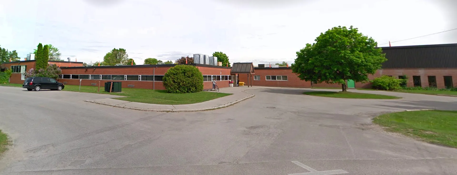 L'edificio in mattoni della Elmvale District High School, con un prato e alberi in primo piano, è circondato da un viale pavimentato e da altri edifici sullo sfondo.