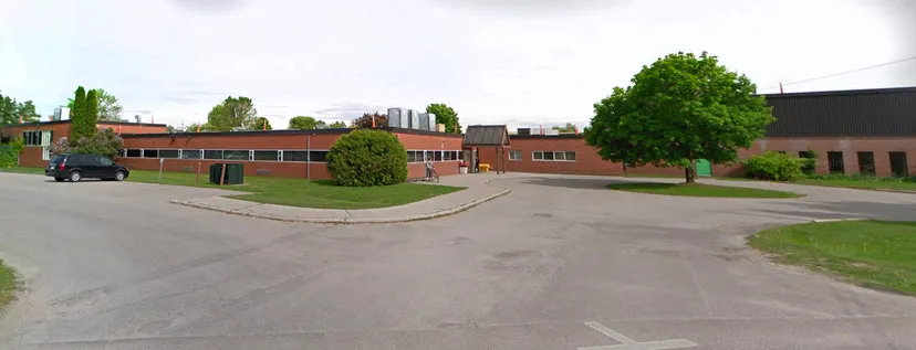 L'edificio in mattoni della Elmvale District High School, con un prato e alberi in primo piano, è circondato da un viale pavimentato e da altri edifici sullo sfondo.