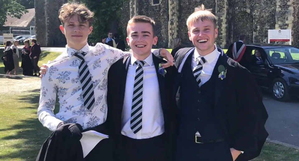 Tre studenti in divisa scolastica all'aperto nel campus del Dover College mentre ridono.