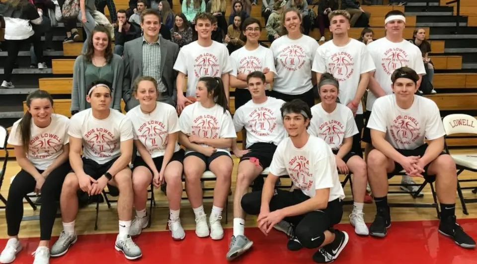 Un gruppo di studenti della Lowell High School è seduto in una palestra e indossa magliette sportive bianche uniformi.