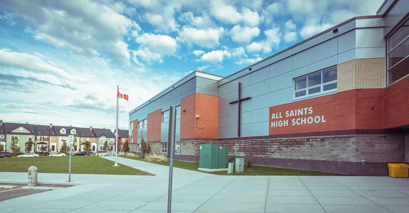L'edificio moderno in mattoni e vetro della All Saints High School a Calgary sotto un cielo nuvoloso con un'area esterna ben curata.
