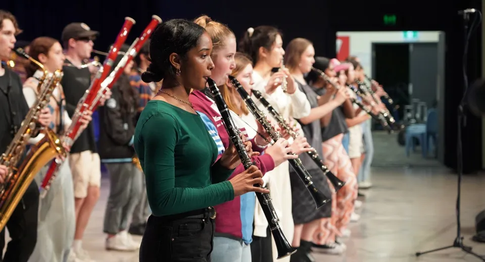 Studenti e studentesse del John Paul College suonano strumenti a fiato su un palco durante un concerto.