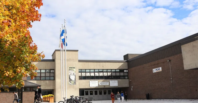 L'edificio in mattoni con un'alta torre della Pierrefonds Community High School è circondato da alberi dal fogliame autunnale.