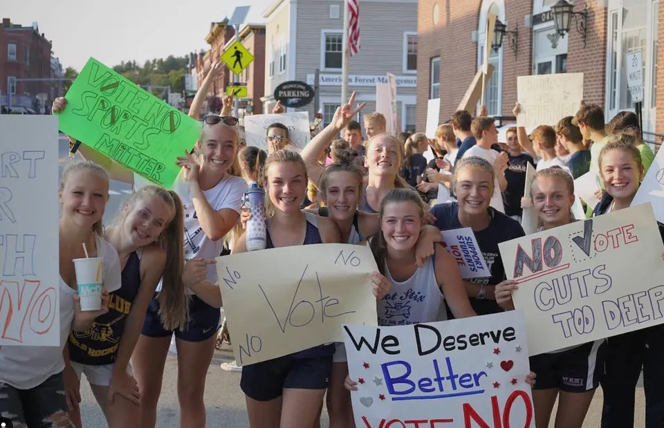 Studentesse e studenti della Mount Blue High School si riuniscono in una strada tenendo cartelli con messaggi politici.