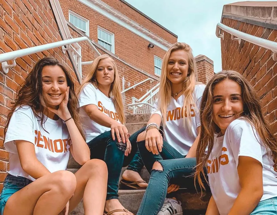 Quattro studentesse sedute davanti a un edificio in mattoni con decorazioni bianche nel campus della Newburyport High School.