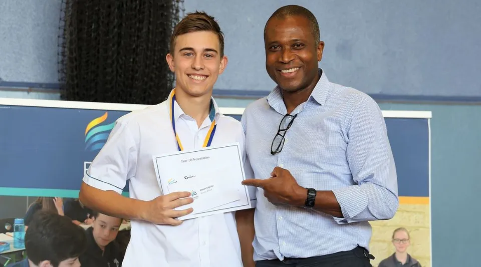 Uno studente del Kinross College tiene in mano un certificato ed è in piedi accanto a un uomo anziano.