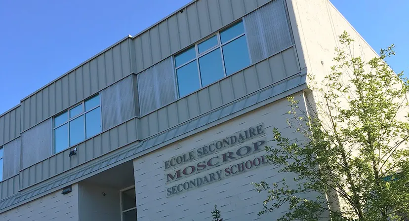 L'edificio scolastico moderno della Moscrop School, con grandi finestre e una scritta ben visibile, è circondato da alberi.
