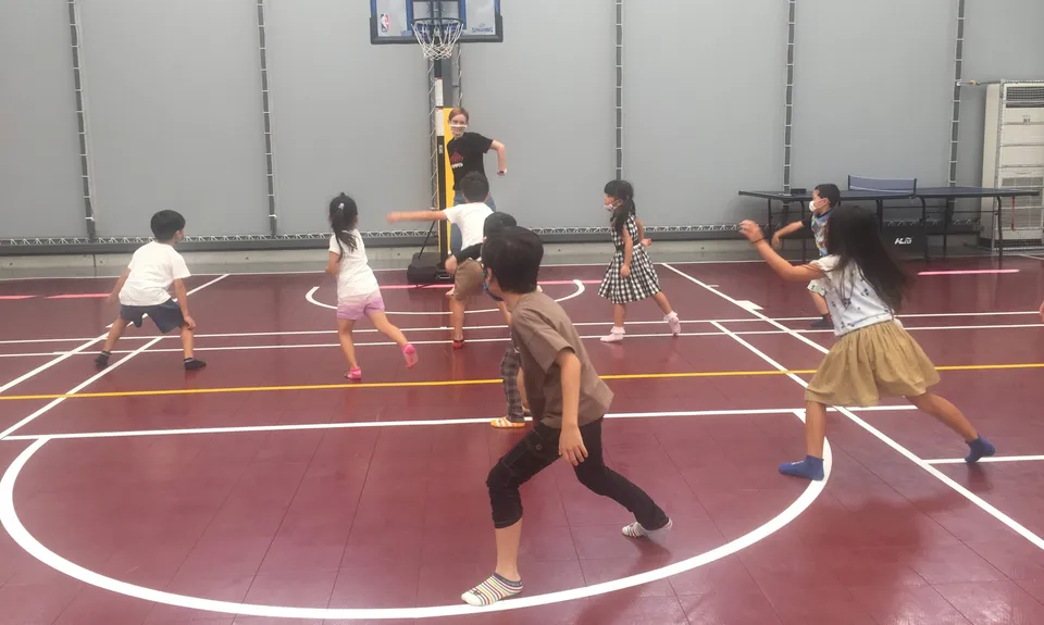 Kinder der Ascot International School bewegen sich auf einem Spielfeld in der Sporthalle.