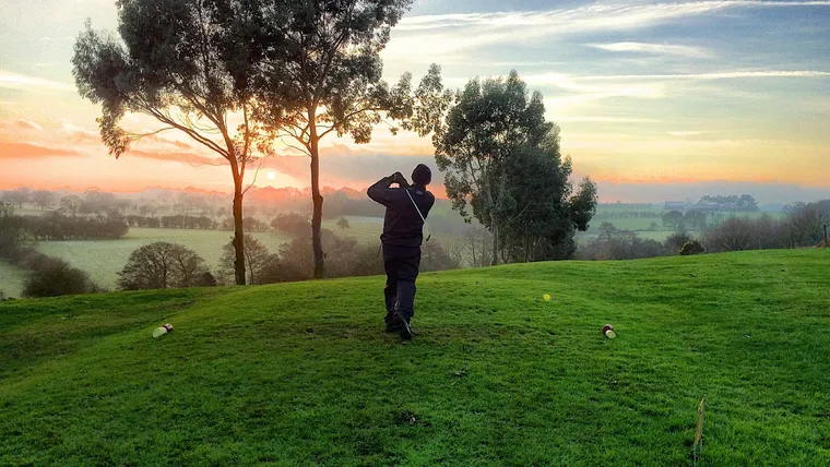Golfspieler schlägt bei Sonnenaufgang auf einer Wiese mit Bäumen ab