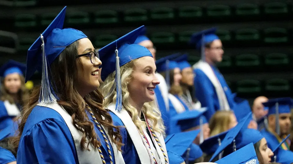 Un gruppo di diplomati con toghe e tocchi blu è in posa insieme su uno sfondo scuro nella foto di diploma del Poudre School District.