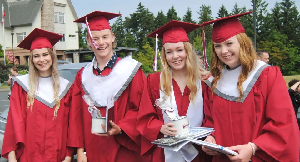 Un gruppo di diplomati della Pender Harbour Secondary si trova all'aperto con toghe e tocchi rossi davanti a uno sfondo alberato.