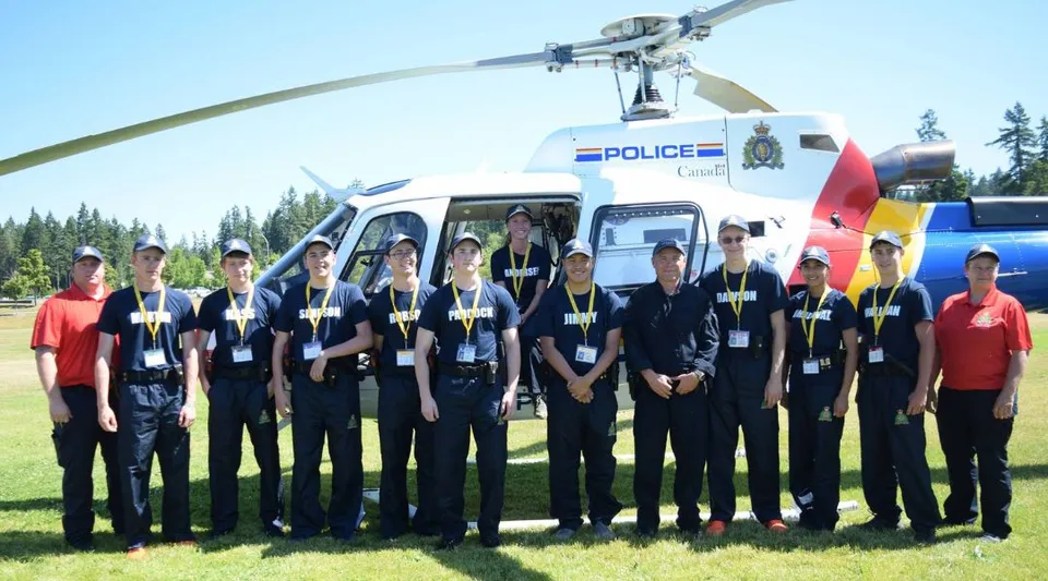 Un gruppo di agenti di polizia si trova davanti a un elicottero della polizia su un prato nel campus della Alberni District Secondary School.