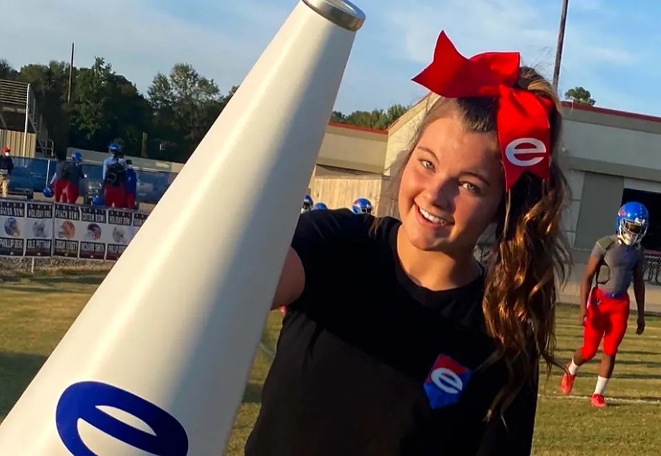 Una giovane donna con un fiocco rosso tra i capelli sorride davanti al campo sportivo della Evangel Christian Academy.