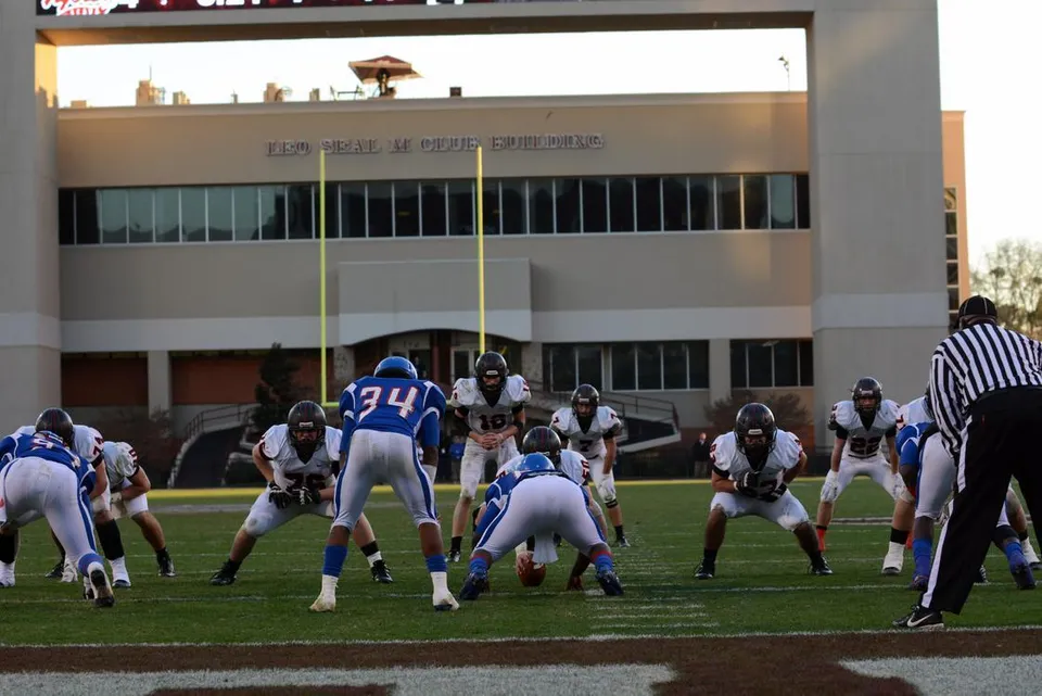 Giocatori di football americano della Saint Stanislaus Catholic High School si schierano sul campo davanti a un edificio.