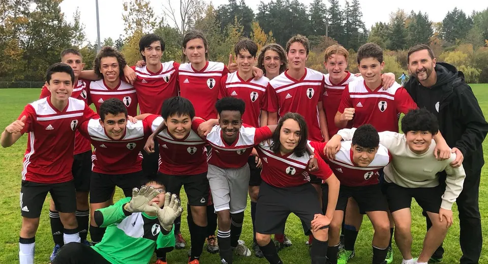 Un gruppo di studenti della Esquimalt High School posa insieme su un campo da gioco con alberi sullo sfondo.