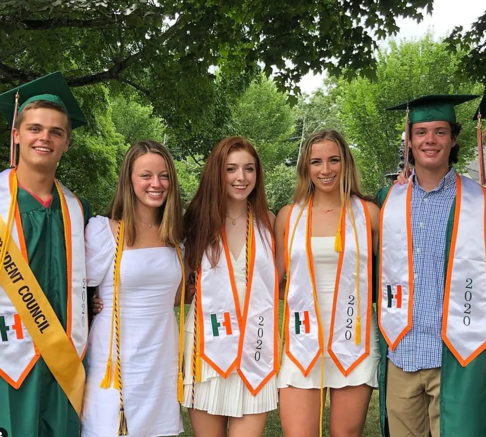 Cinque studenti in abiti da laurea in piedi insieme nel verde nel campus della Hopkinton High School.