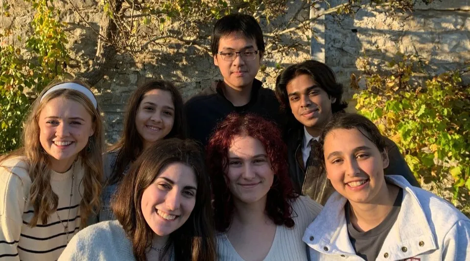 Un gruppo di studenti e studentesse posa davanti a un muro di pietra all'interno del terreno del UWC Atlantic College.