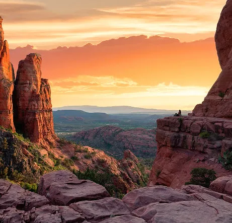 Formaciones de roca roja al atardecer con una persona sentada en un saliente sobre el valle