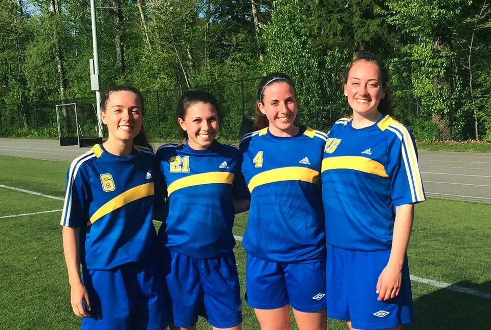 Quattro studentesse della Sutherland Secondary School si trovano insieme su un campo erboso indossando divise sportive blu e gialle.